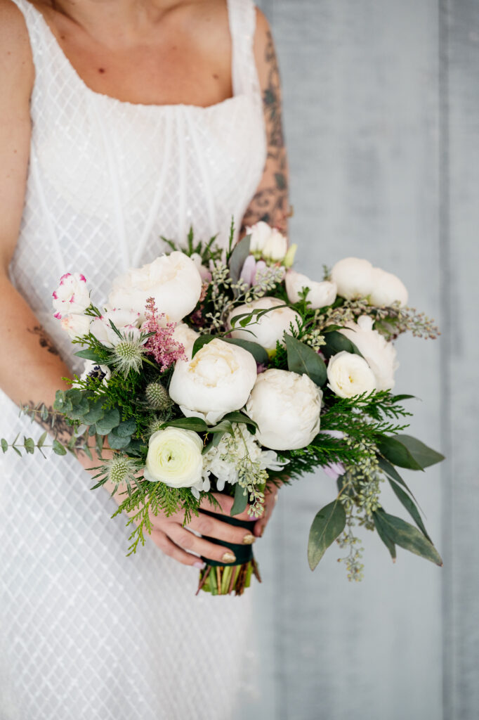 Close up of a bridal bouquet featuring classic white blooms wiht a touch of evergreen sprigs. 