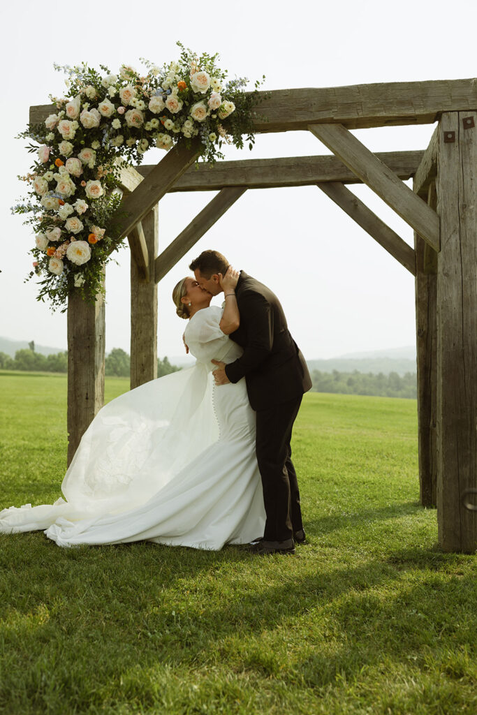 Couple getting married and sharing a sweet kiss underneath their arbor that is decorated with lush wedding florals. 