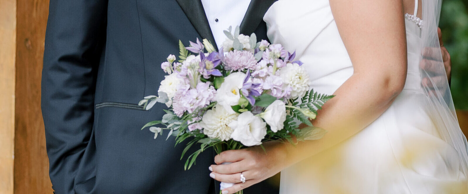 A shot of a couple featuring a purple and white bridal bouquet.