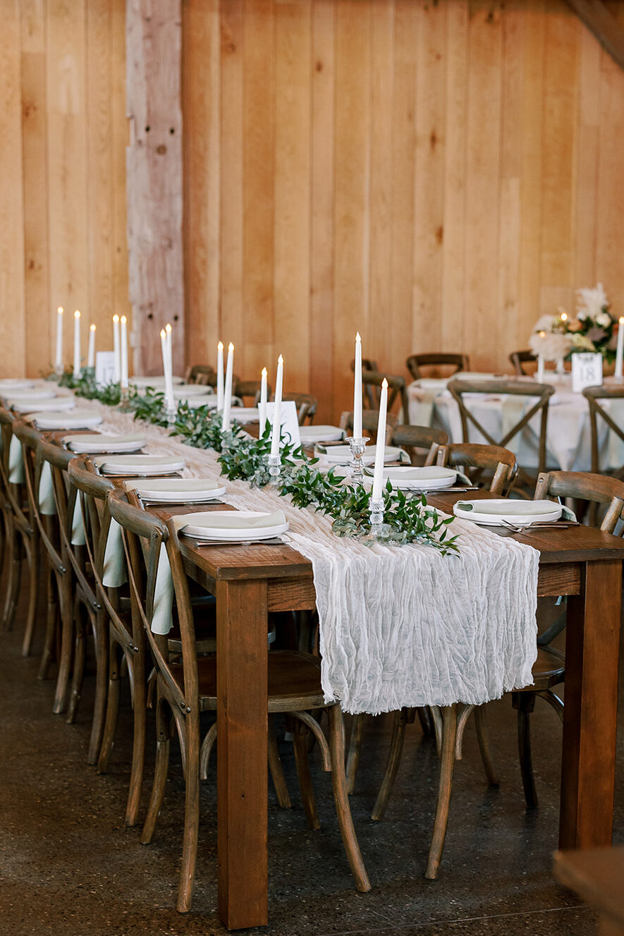A beautiful farmhouse tablescape featuring muted sage linen napkins,  cream linens, greenery and candles through the center. 
